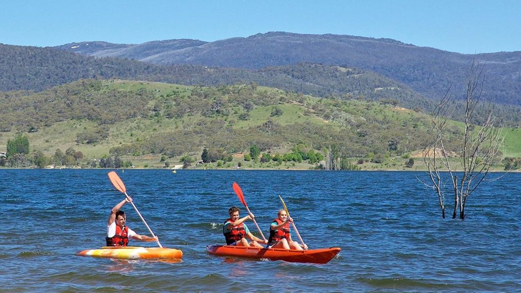 Kayakers paddling across Lake Jindabyne with the mountains and green countryside in the background.