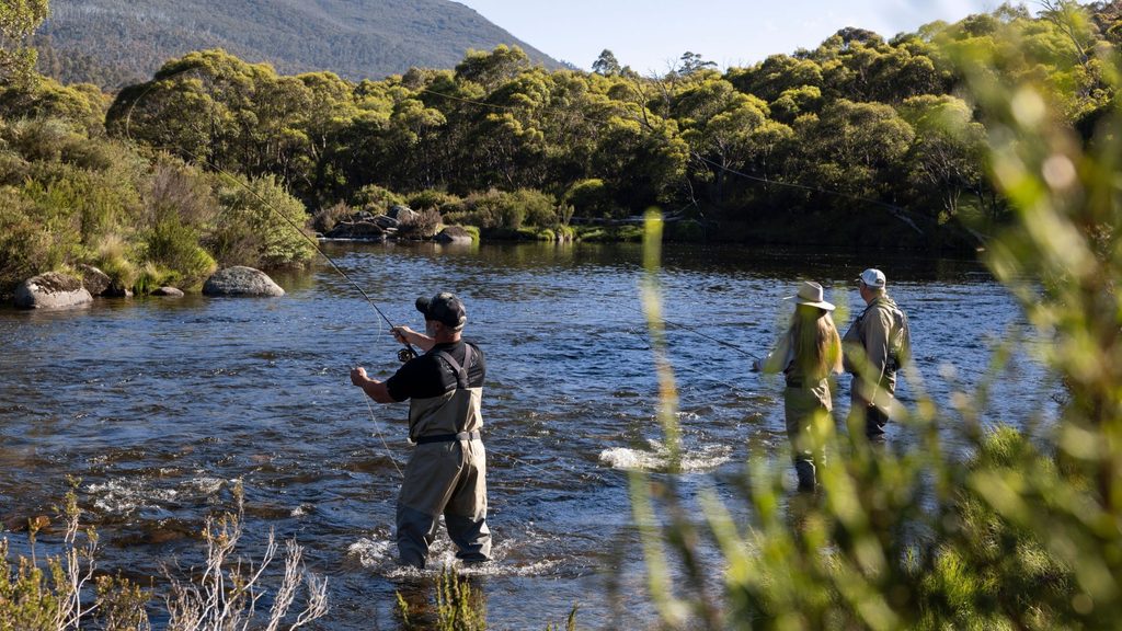 Three people fly fishing in a mountain river surrounded by native bushland in the Snowy Mountains, NSW.